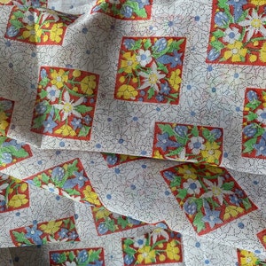 May include: White fabric with a repeating pattern of red, yellow, and blue floral designs. The floral designs are in a diamond shape and are surrounded by a white background with small blue dots.