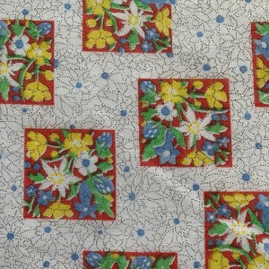 May include: White fabric with a repeating pattern of red, yellow, blue, and green floral squares. The flowers are stylized and have a vintage look.
