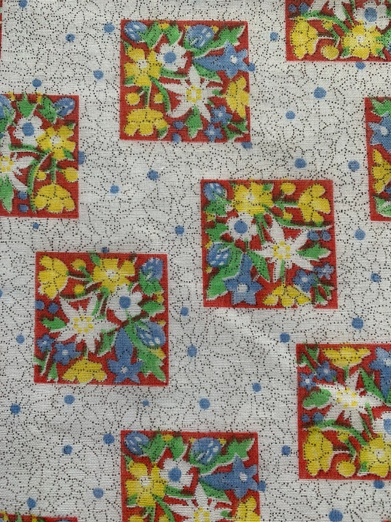 May include: White fabric with a repeating pattern of red, yellow, blue, and green floral squares. The flowers are stylized and have a vintage look.
