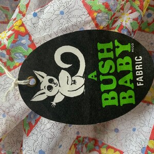May include: A black and white oval tag with a cartoon possum and the text "A BUSH BABY FABRIC REGD" in green and white lettering.