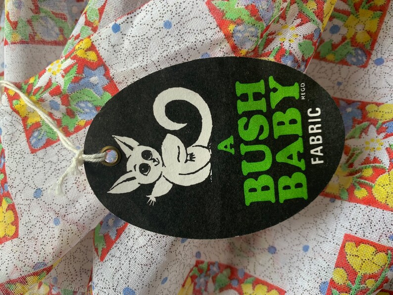 May include: A black and white oval tag with a cartoon possum and the text "A BUSH BABY FABRIC REGD" in green and white lettering.