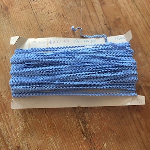 May include: A spool of light blue trim with a white label that reads "74-ses yos 4077/49 130".