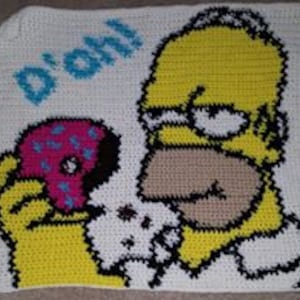 Op de afbeelding: Een gehaakt vierkant met een cartoon afbeelding van Homer Simpson uit The Simpsons, die een roze donut eet. De tekst "D'oh!" staat in blauw boven Homers hoofd.