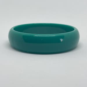 May include: A teal-colored bangle bracelet. The bracelet is a solid, smooth band with a rounded shape. The color is a vibrant, saturated teal, and the surface appears glossy. This accessory is suitable for everyday wear.