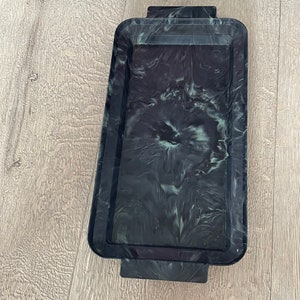 May include: A rectangular tray with a marbled black and white design. The tray has a raised edge and two rectangular handles. The tray is made of a solid material and is suitable for serving or display.