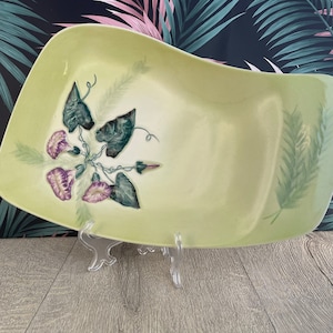 Peut inclure: Un plat de service rectangulaire en céramique vert clair avec un bord incurvé. Il est orné de fleurs de gloire du matin violettes et blanches et de feuilles vertes. Un motif de fougère est peint sur le côté droit.