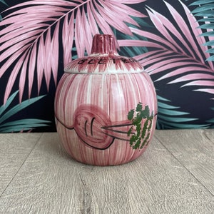May include: A vintage ceramic beet jar with a lid. The jar is pink with white stripes and a beet illustration. The lid and top of the jar are a darker pink. The word "BEET" is written on the lid.