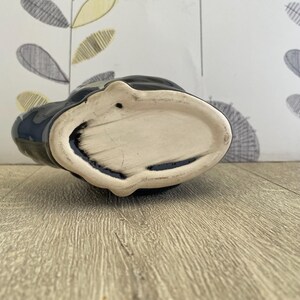 May include: A black ceramic vase with a cream-colored interior. The vase has a unique shape and a glossy finish. The bottom of the vase is visible, showing its oval shape and the texture of the ceramic.