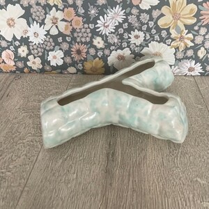 May include: A Y-shaped ceramic planter with a glossy finish, featuring a pale mint green and white mottled glaze. The object has a hollow centre and a textured, segmented surface that resembles a branch or a natural organic form.