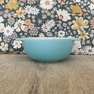 May include: A solid light blue ceramic bowl with two small side handles. The bowl features a smooth, matte finish and a rounded, deep basin design, providing a simple and functional vessel for serving or preparing various food items in the kitchen.