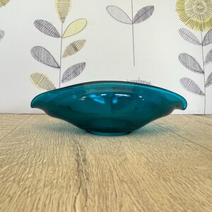 May include: A translucent teal glass bowl with an elongated, oval shape and pointed ends. The bowl features smooth, curved edges and a deep, rounded base, showcasing a vibrant, solid colour throughout the entire glass structure.