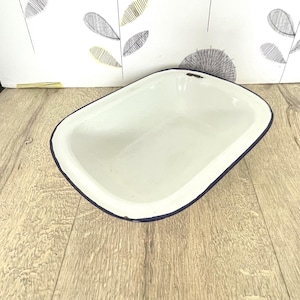 May include: White enamel baking dish with a blue rim. The dish is oval shaped and has a slight curve to the sides.