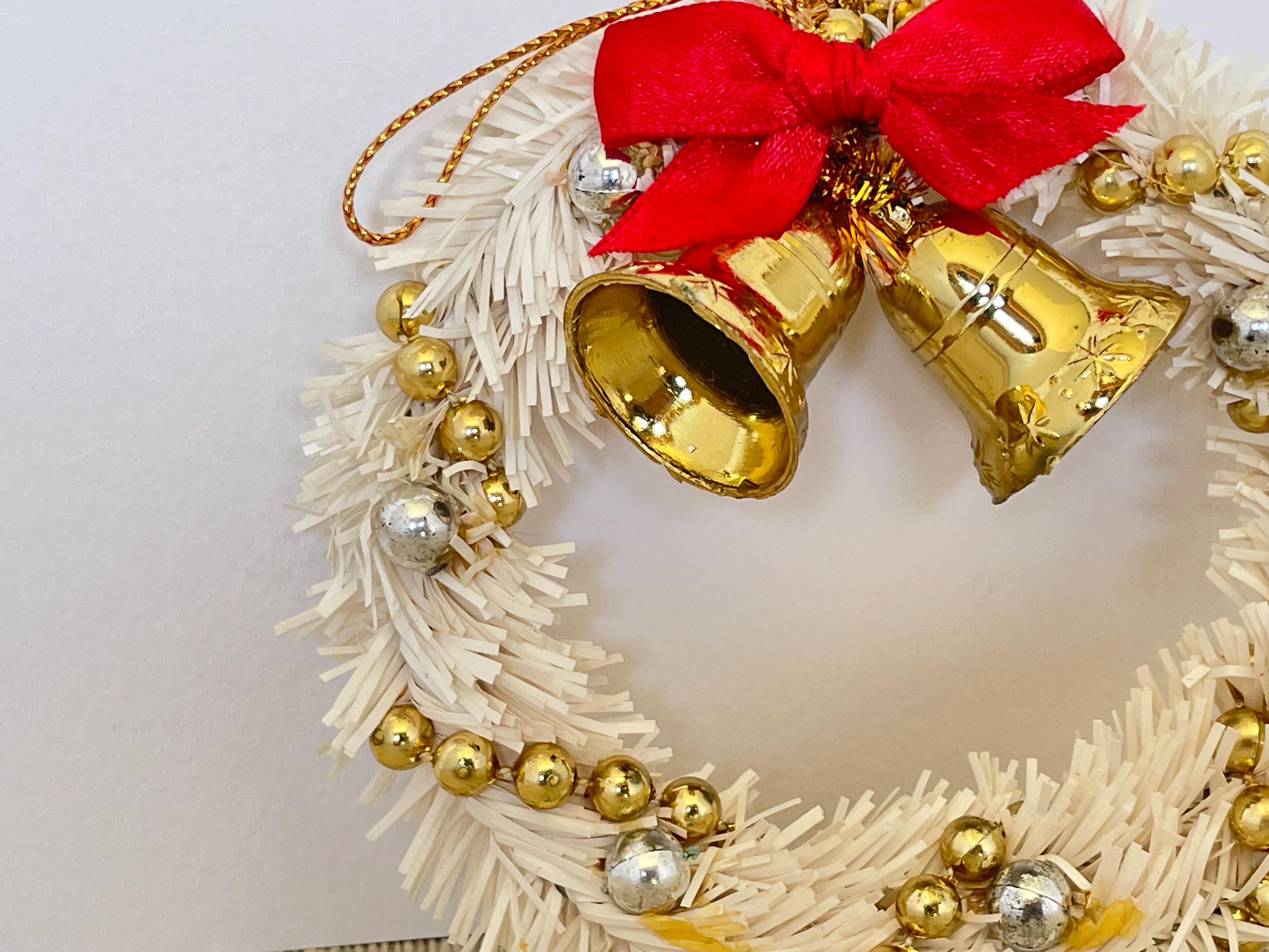 金色のベルと赤いリボンが付いた白いミニティンセルクリスマスリース