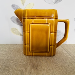 May include: A brown ceramic jug with a geometric design. The jug has a handle and a spout.