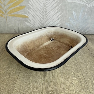 Könnte beinhalten: Eine ovale Schale aus cremefarbener Keramik mit braunem Innenraum und schwarzem Rand. Die Schale hat ein rustikales, strukturiertes Aussehen. Sie steht auf einer hellen Holzoberfläche. Abmessungen: ca. 30 cm lang.