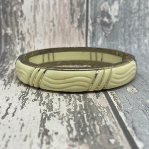 May include: A white plastic bangle bracelet with a gold trim and a wavy design.