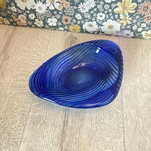 May include: A vibrant blue glass bowl with a unique, organic shape. The bowl features a swirling, textured design that creates a captivating visual effect. This decorative piece is perfect for displaying small items or as a standalone art object.