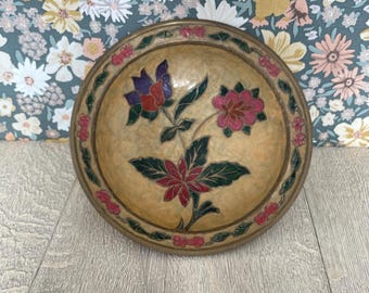 May include: A round, decorative bowl with a floral design. The bowl has a gold-colored rim and a beige interior. The floral design features red, pink, and purple flowers with green leaves.
