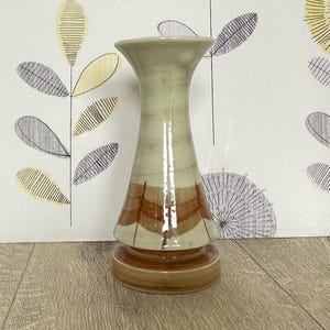 May include: A ceramic vase with a flared top and a wide base. The vase features a light beige and brown colour scheme with a decorative pattern in the middle. The vase is approximately 25 cm tall.