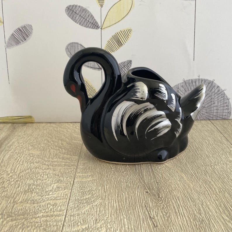 May include: A black ceramic swan figurine with white and gray accents on the wings. The swan has a curved neck and a red beak. The figurine is a decorative item, likely for home decor.