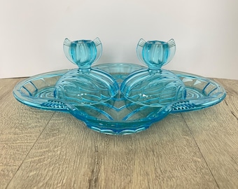 May include: A blue glass serving tray with two matching lidded dishes. The tray is shaped like a heart and has a decorative design. The dishes are also heart-shaped and have a swirl design.