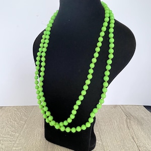 May include: A long, bright green beaded necklace displayed on a black mannequin. The necklace is made up of many round beads, creating a bold and vibrant accessory. The beads are a solid, eye-catching green colour.