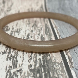 May include: A light brown bangle bracelet. The circular bracelet has a smooth, polished surface. The jewellery is a neutral colour that would complement many outfits.