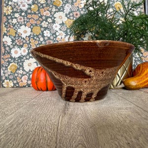 May include: A wide, deep ceramic bowl with a glossy dark brown glaze. The exterior features a textured, lighter brown speckled band that wraps around the center. The bowl has a smooth, rounded rim and a tapered base, showcasing a handcrafted finish.