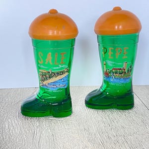 以下が含まれることがあります： オレンジ色の蓋が付いた、緑色のガラス製のブーツ型ソルト＆ペッパーシェーカー2つ。片方には緑色で「SALE」、もう片方には「PEPE」と書かれています。どちらもリビエラ・アドリアティカのビーチシーンが描かれています。