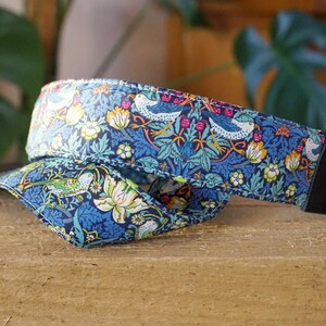 May include: A blue and green camera strap with a floral pattern and birds. The strap is made of fabric and has a black leather adjustable strap.