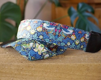 May include: A blue and green camera strap with a floral pattern and birds. The strap is made of fabric and has a black leather adjustable strap.