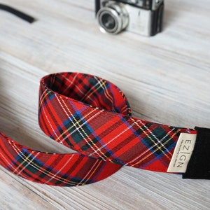 May include: Red and black plaid camera strap with a black leather adjustable strap and a brown label that says "EZ|IGN".