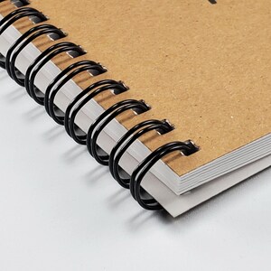 May include: Close-up of a brown notebook with black wire-o binding. The notebook has a textured cover and is closed.