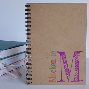 Personalized notebook with brown kraft cover and a colorful name and monogram initial in the lower right side of the cover. These custom notebooks are great for girls or boys, and women. Perfect gift idea for party favors, students and teachers.