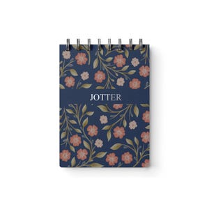May include: A spiral-bound notepad with a navy blue cover featuring a floral pattern of peach and light pink flowers with green leaves. The word "JOTTER" is printed in white on a navy blue banner.