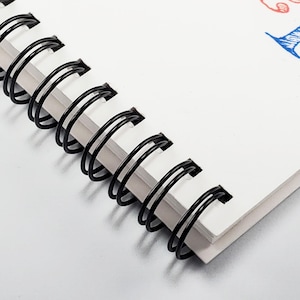 Peut inclure: Gros plan sur une reliure &agrave; spirale noire sur un carnet blanc. La reliure est en m&eacute;tal et a une forme de spirale.