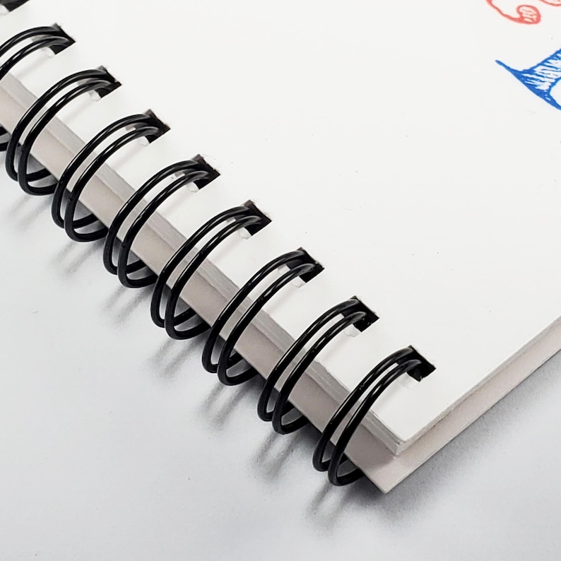 Peut inclure: Gros plan sur une reliure &agrave; spirale noire sur un carnet blanc. La reliure est en m&eacute;tal et a une forme de spirale.