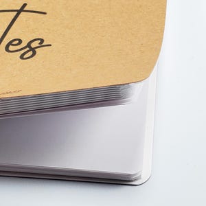May include: Close-up of a brown cardboard notebook with the word "Notes" written in black ink. The notebook is open, revealing white lined pages.