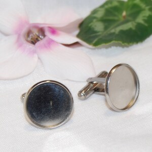 May include: A pair of silver cufflinks with round, clear glass inserts. The cufflinks are on a white surface.