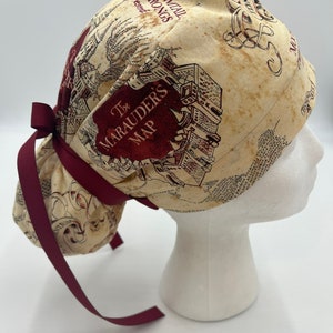 Könnte beinhalten: Eine chirurgische Mütze in Marone und Beige mit einer Schleife. Die Mütze zeigt einen Druck der Karte der Marauder aus der Harry-Potter-Reihe. Die Karte zeigt den Grundriss von Hogwarts und enthält den Text "The Marauder's Map" und "I solemnly swear that I am up to no good."