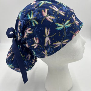 Puede incluir: Un gorro de quirófano azul con estampado de libélulas. El gorro tiene un lazo en la parte posterior para una coleta.