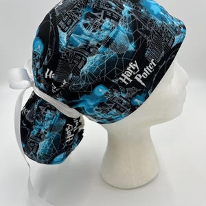 Op de afbeelding: Een zwart-blauwe scrubcap met het opschrift "Harry Potter". De cap heeft een witte strik aan de achterkant. Het patroon bevat architectonische ontwerpen en geometrische vormen.