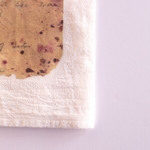 May include: A white towel with a brown and pink stained piece of paper on top. The paper has handwritten text on it.