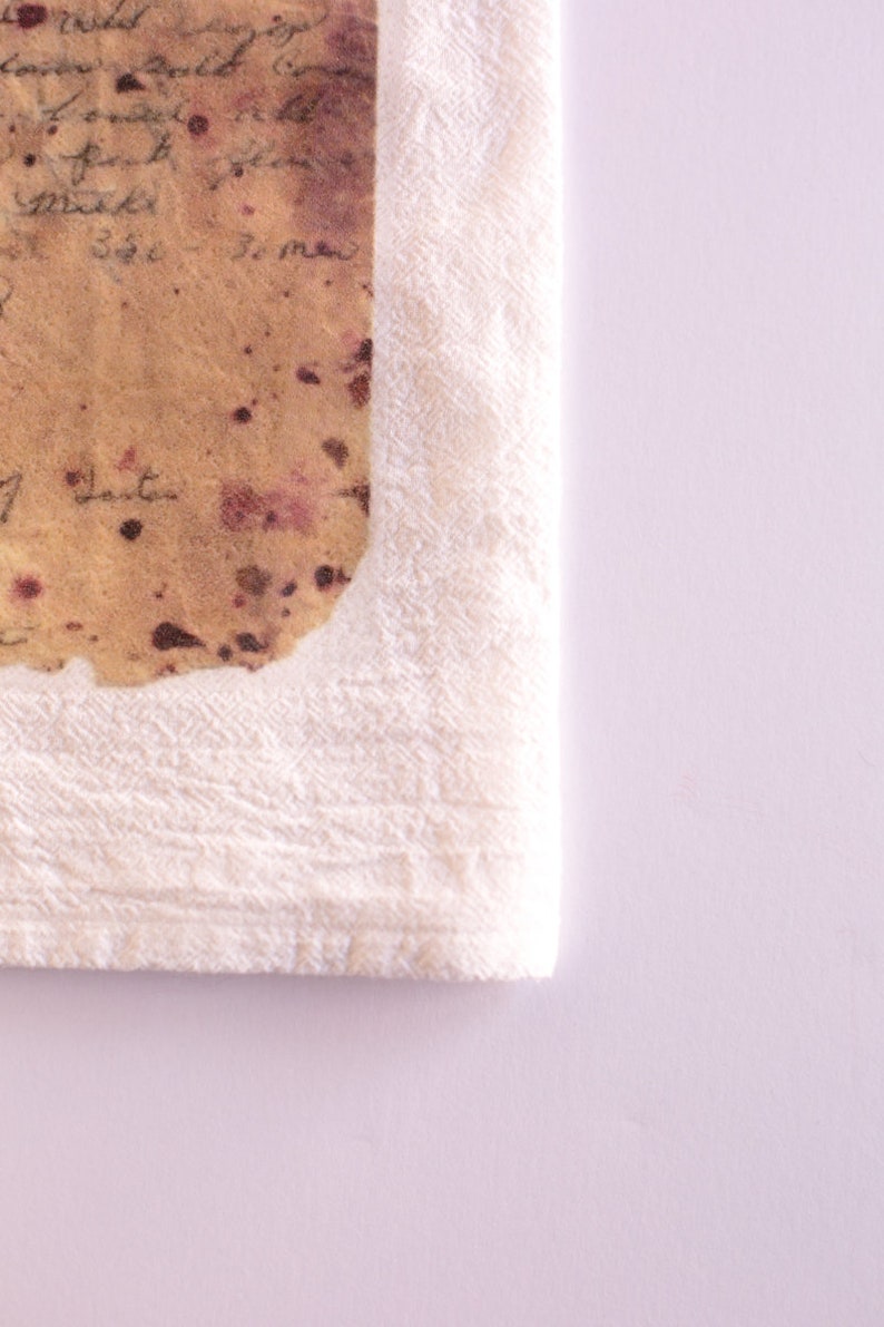 May include: A white towel with a brown and pink stained piece of paper on top. The paper has handwritten text on it.
