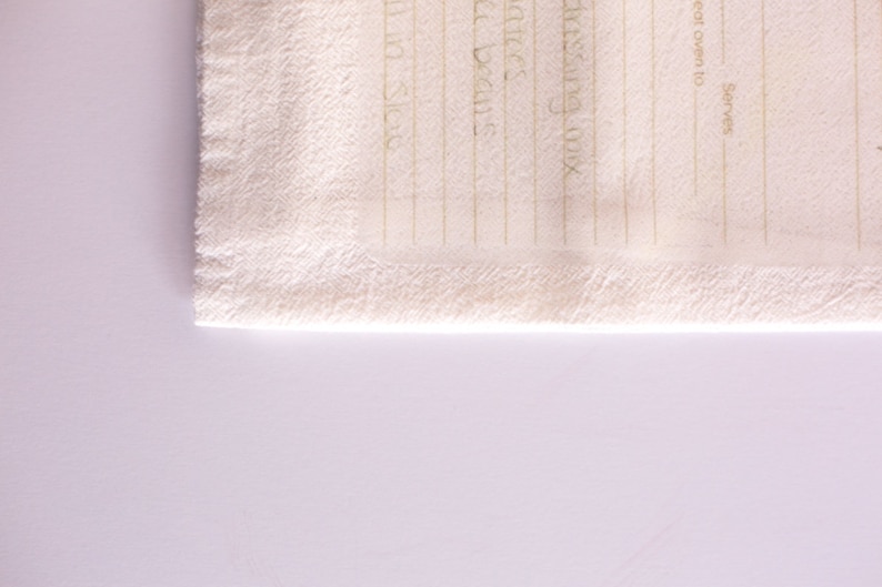 May include: A white kitchen towel with a blank recipe template printed on it. The template has lines for ingredients and instructions, as well as spaces for the name of the recipe, the oven temperature, and the number of servings.