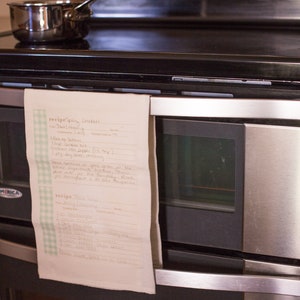 May include: A handwritten recipe for "Spicy Cookies" and "Bliss Balls" is taped to a stainless steel oven. The recipe includes ingredients like "1 bag oats", "1 tsp vanilla", and "1/2 cup cocoa powder".