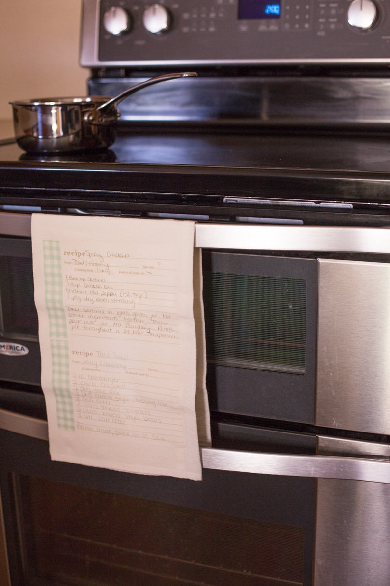 May include: A handwritten recipe for "Spicy Cookies" and "Bliss Balls" is taped to a stainless steel oven. The recipe includes ingredients like "1 bag oats", "1 tsp vanilla", and "1/2 cup cocoa powder".