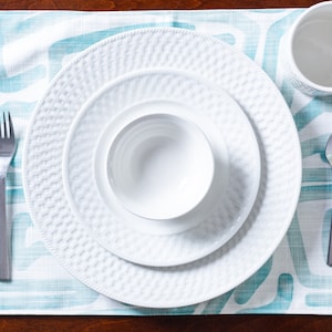 May include: A white dinner plate set with a bowl, fork, and spoon on a blue and white patterned placemat.