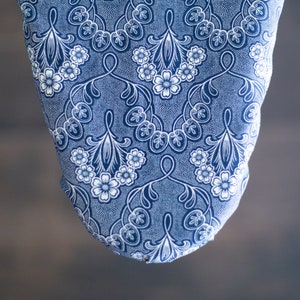 May include: A blue and white patterned ironing board cover with a floral design.