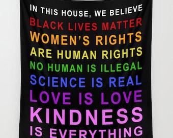 May include: Black wall hanging with the text "IN THIS HOUSE, WE BELIEVE" and statements in rainbow colours. The statements include "BLACK LIVES MATTER", "WOMEN'S RIGHTS", and "LOVE IS LOVE".